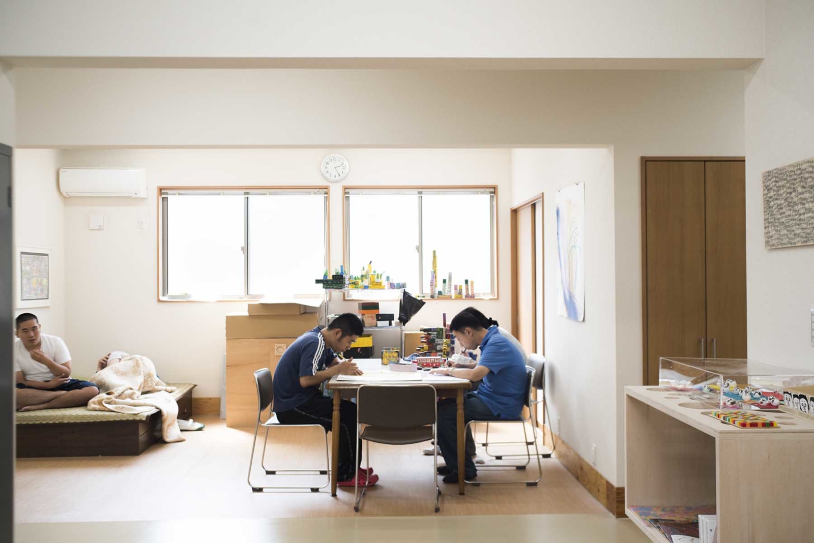 【写真】奥に窓が２つある部屋で２人の人物が向かい合って机で作業している。