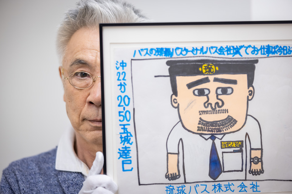 [Photograph]狩俣明宏さんの作品を手にこちらを見つめるイッセー尾形さん