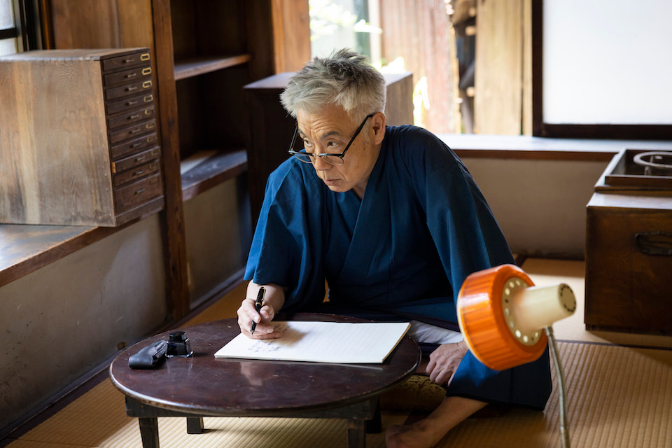 [Photograph]書きながら、右横をにらんでいるイッセー尾形さん。