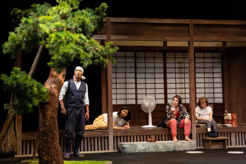 男性1名、女性2人、隆子の4名が家の縁側に座り、全員が庭の木の方を眺めている写真。