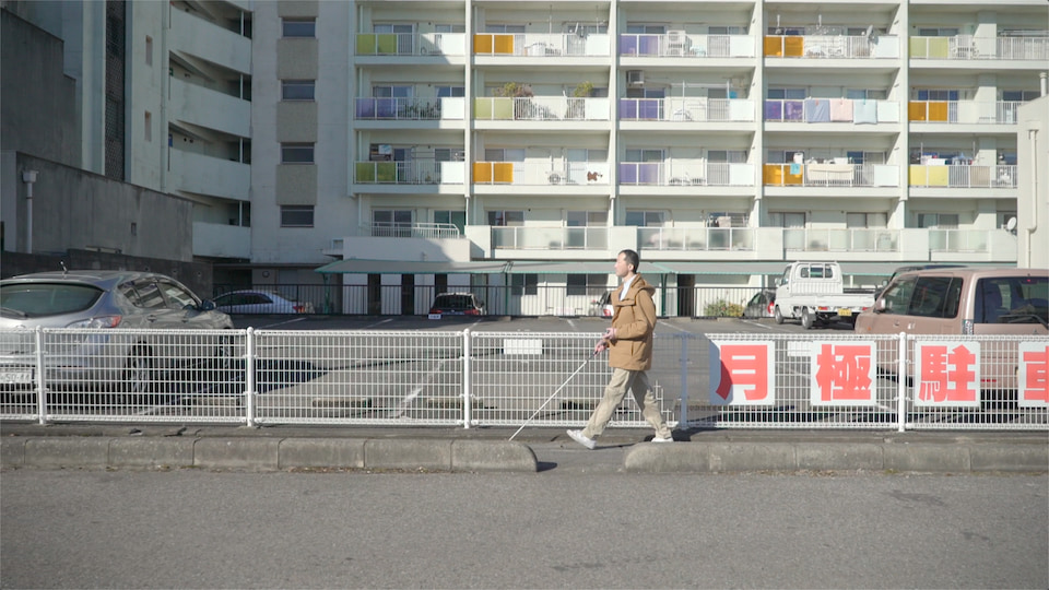 白杖を手に、団地の横の路をひとり歩く白鳥さん。