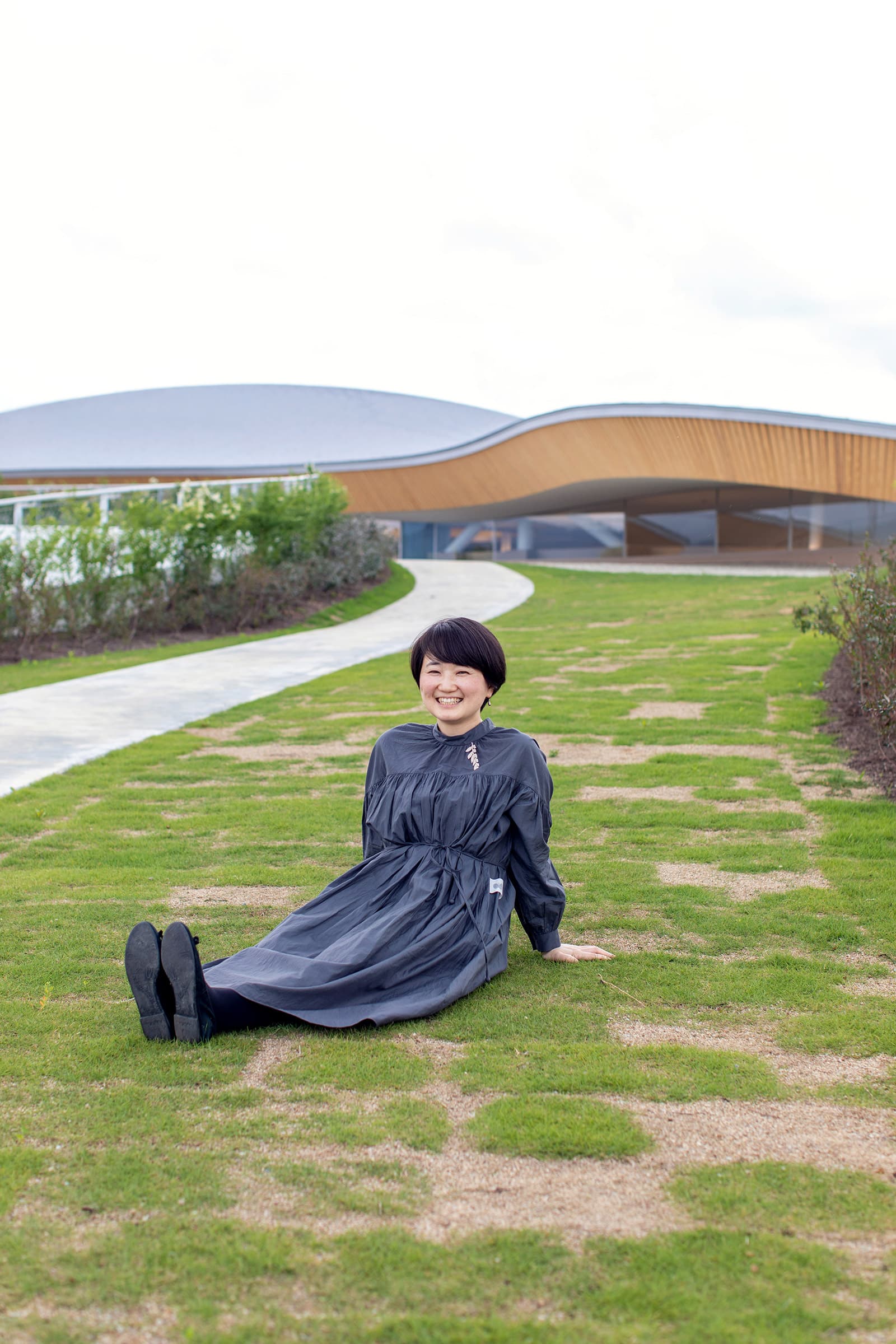 【写真】敷地内の広場にて座って笑う大西麻貴さん