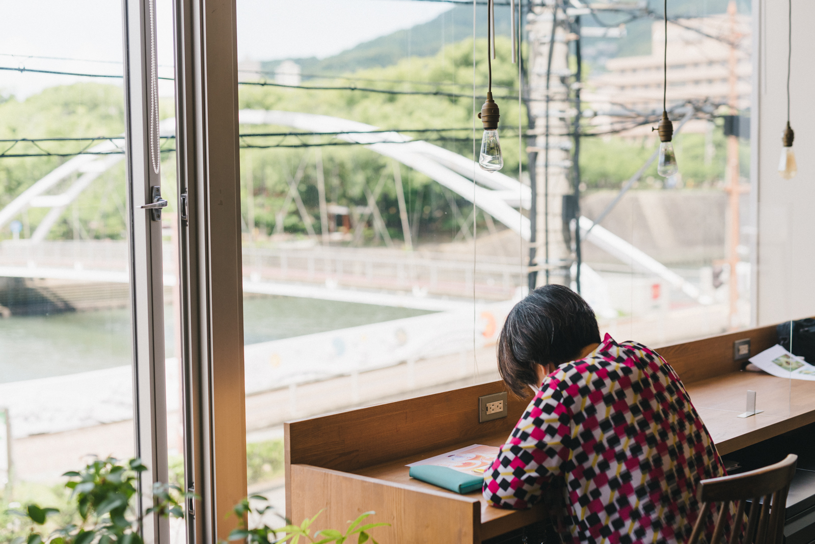 [Photograph]目の前に川と緑が見える、いつもの席で制作中のmegumiさん