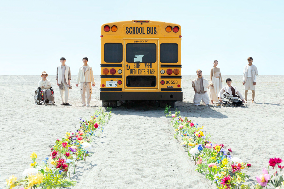【写真】caravanイメージ画像。パフォーマーたちが黄色いスクールバスの左右に並んでいる。