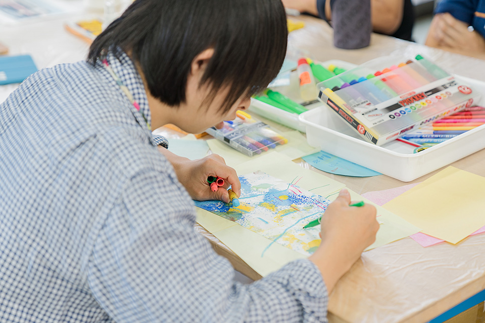 【写真】青い花の絵に緑色のペンで絵を描き加える参加者