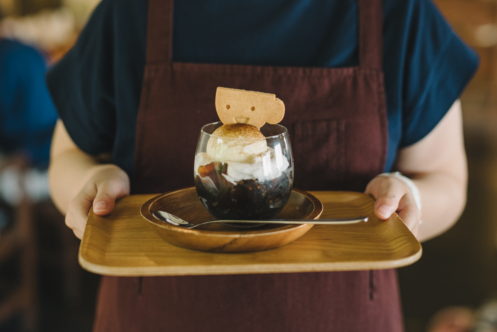 【写真】お盆の上にコーヒーゼリーがある。エプロンをした人がもっている。グラスのなかには、ゼリー、生クリーム、アイスがのり、一番上に笑顔のクッキーがささっている。