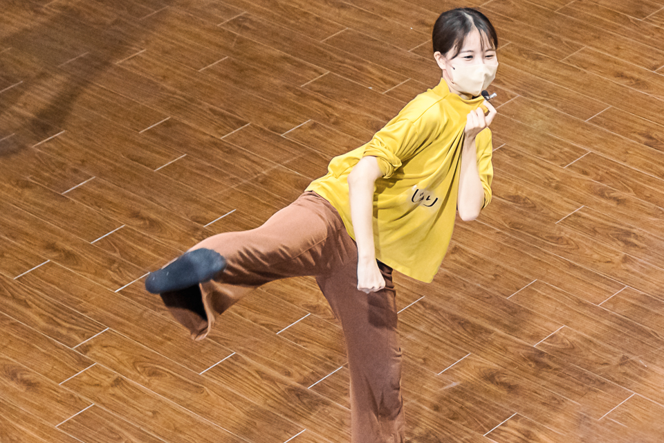 【写真】ダンスクラスで右足を上げてキックしながらマイクで話をする西岡さん