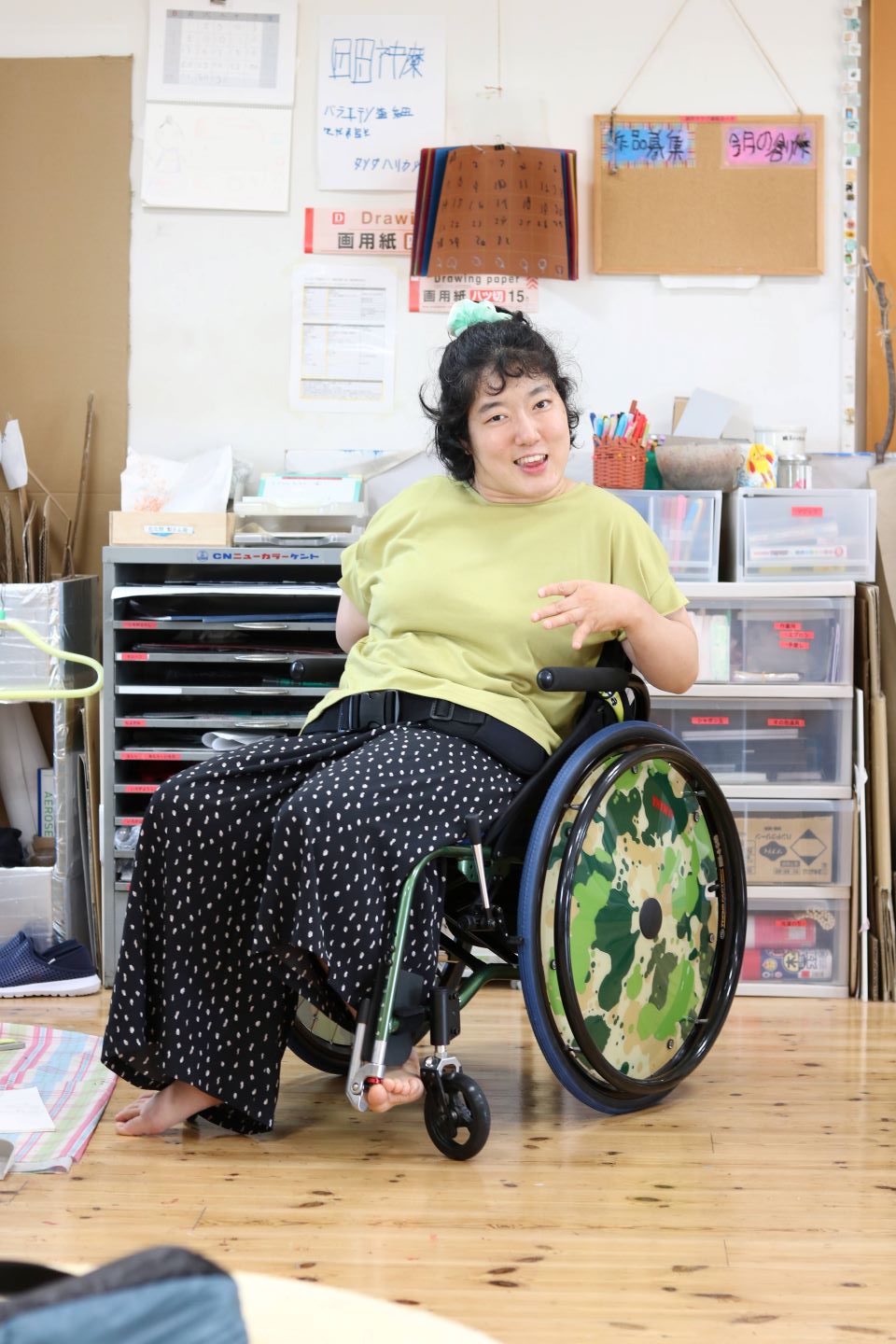 車椅子に乗り、こちらを笑顔で見つめる森さん。背景には使用している制作の道具が見える