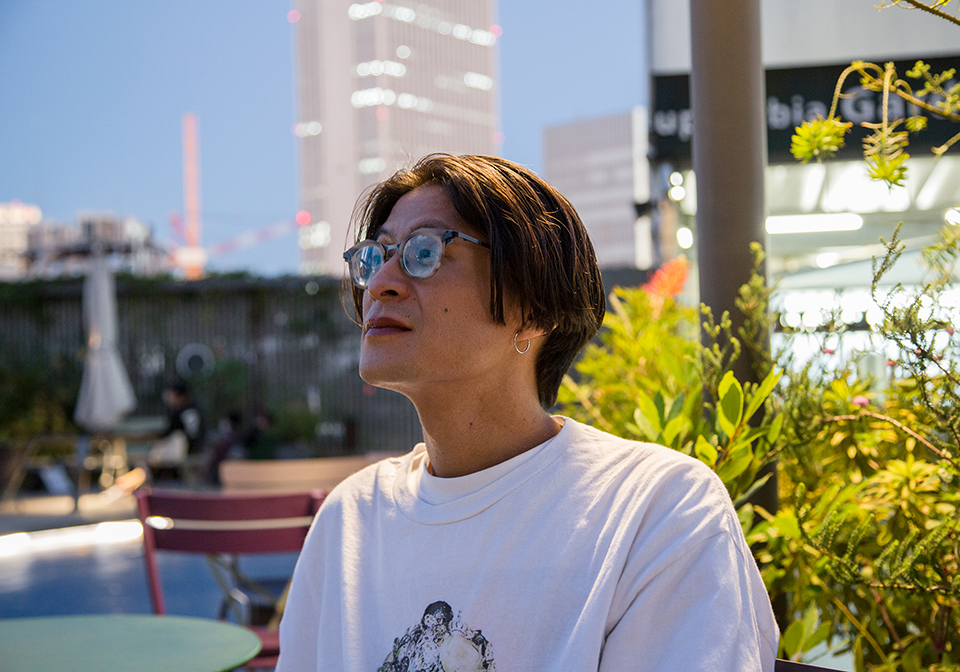 【写真】ビルを背景にしたテラスに座る金川さんが、左手遠方を見つめている様子