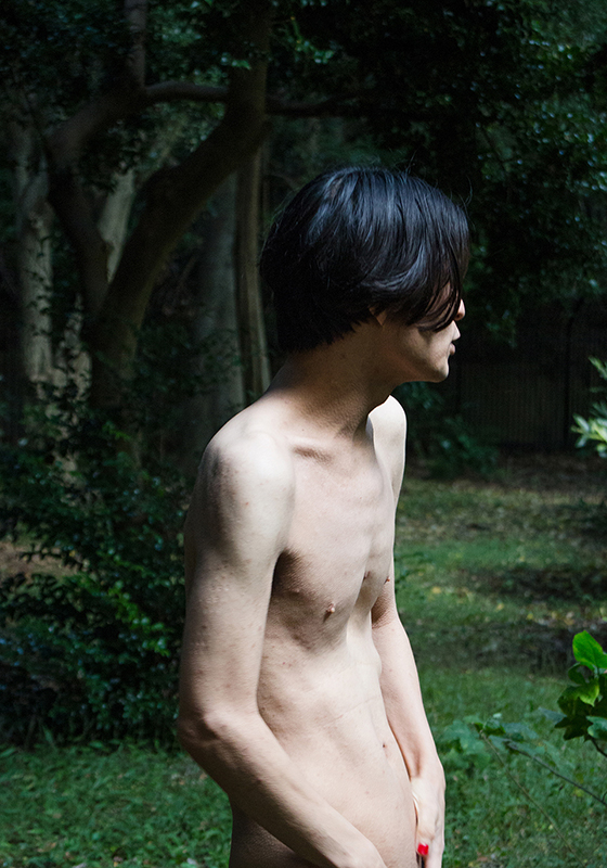 【写真】緑の木々を背景に、顔を背けて裸でたたずむ金川さんの様子