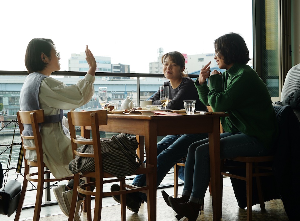 【写真】ケイコと友人2名が、川沿いにあるカフェで楽しそうで手話で話す