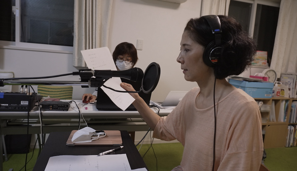 【写真】ヘッドフォンをして彩木さんが音声ガイドをレコーディングしている。その奥には平塚さんの姿