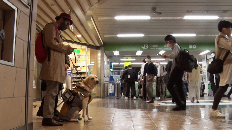 【写真】盲導犬ピースとともに改札の前にたつ難波さん