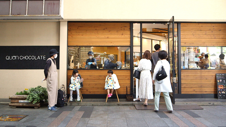 【写真】愛知県豊橋市にある久遠チョコレートの店舗外観。お客さんがどんどん入っていく。店はガラス張りになっていて、チョコレートをつくっているところが外からも見られる