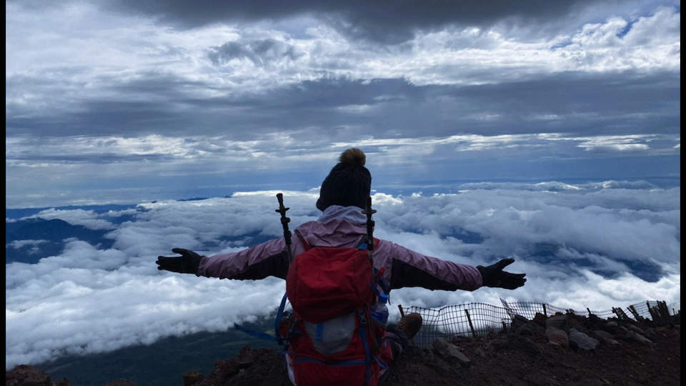 【写真】富士山に登山した鈴木ゆずなさんの後ろ姿。眼下に広がる雲を前に両手を広げている。