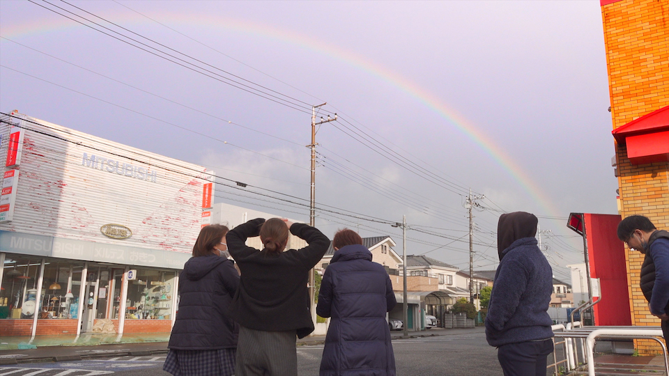 【写真】雨上がりの空に大きな虹がかかっているのを見上げている、地域で共に生きるナノの仲間たちの後ろ姿。