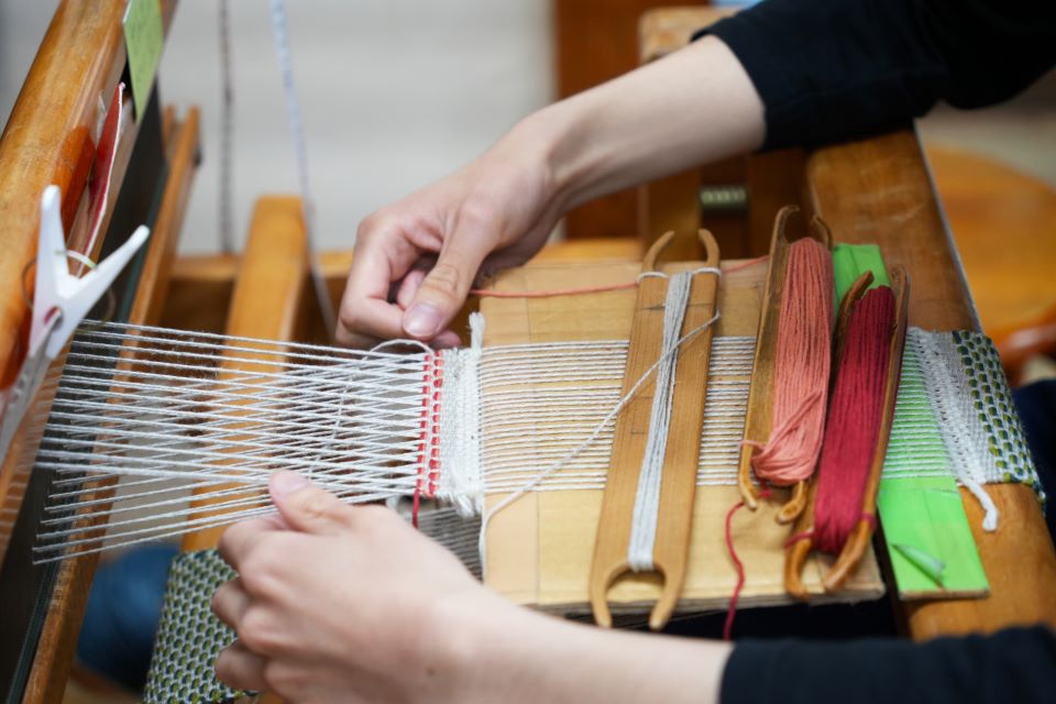 【写真】機織りの道具を使って、３色の糸を織り込んでいる様子