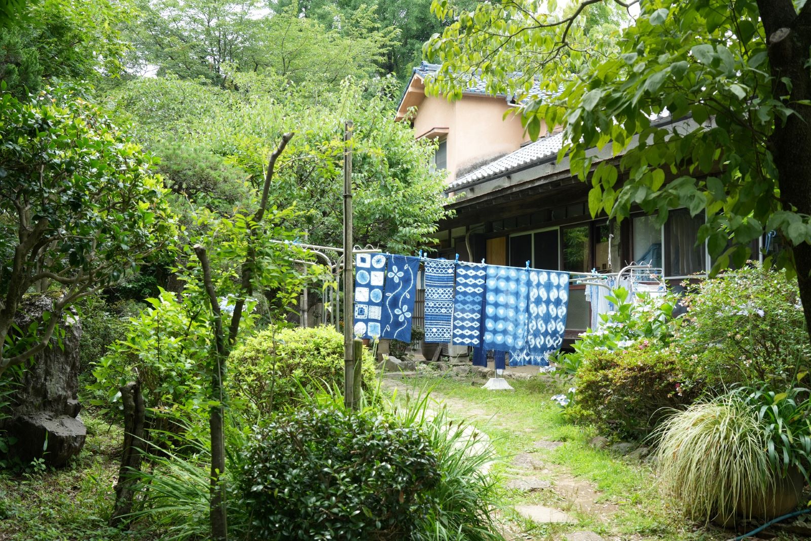 【写真】緑豊かな庭に藍色に染められた布が、干されている風景