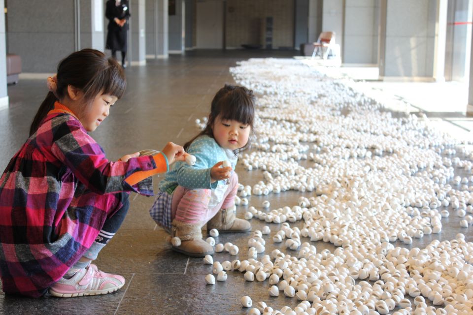 【写真】床半分に、手のひらサイズの白い工作物が一面に広がっている。子供2人がかがんで作品をさわっている。
