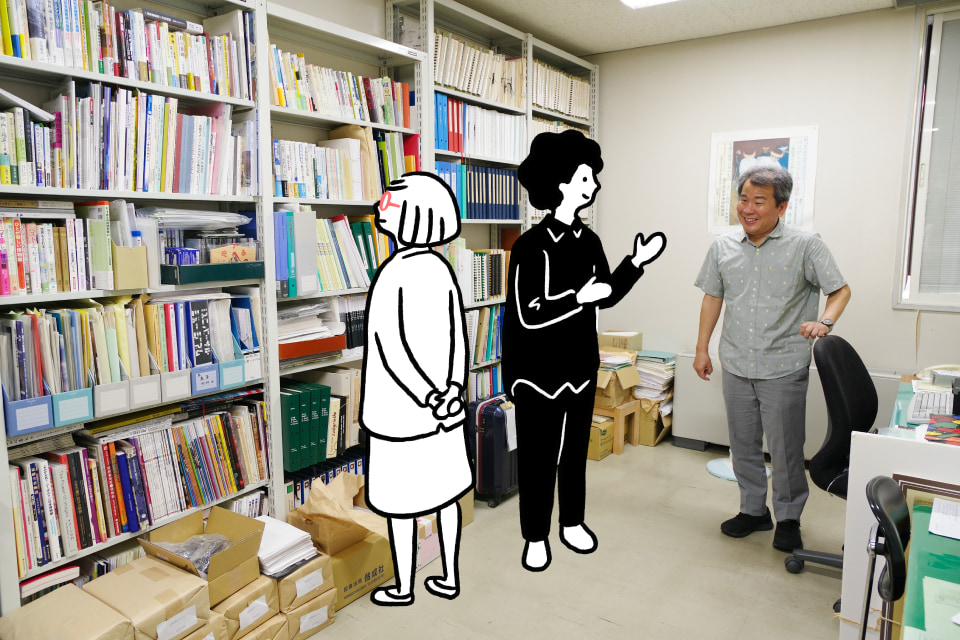 【写真】ぎっしり本が積み込まれた本棚の前に立つ広瀬さんがイラストのダイバーさんとシティさんと会話している。床には梱包された印刷物の束やスーツケースがある。
