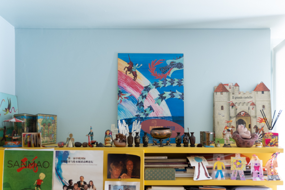 【写真】城の形をした絵本、ドラゴンやユニコーン、虹が描かれた絵本、小さな人形や壺などのオブジェが飾られたオフィスの棚