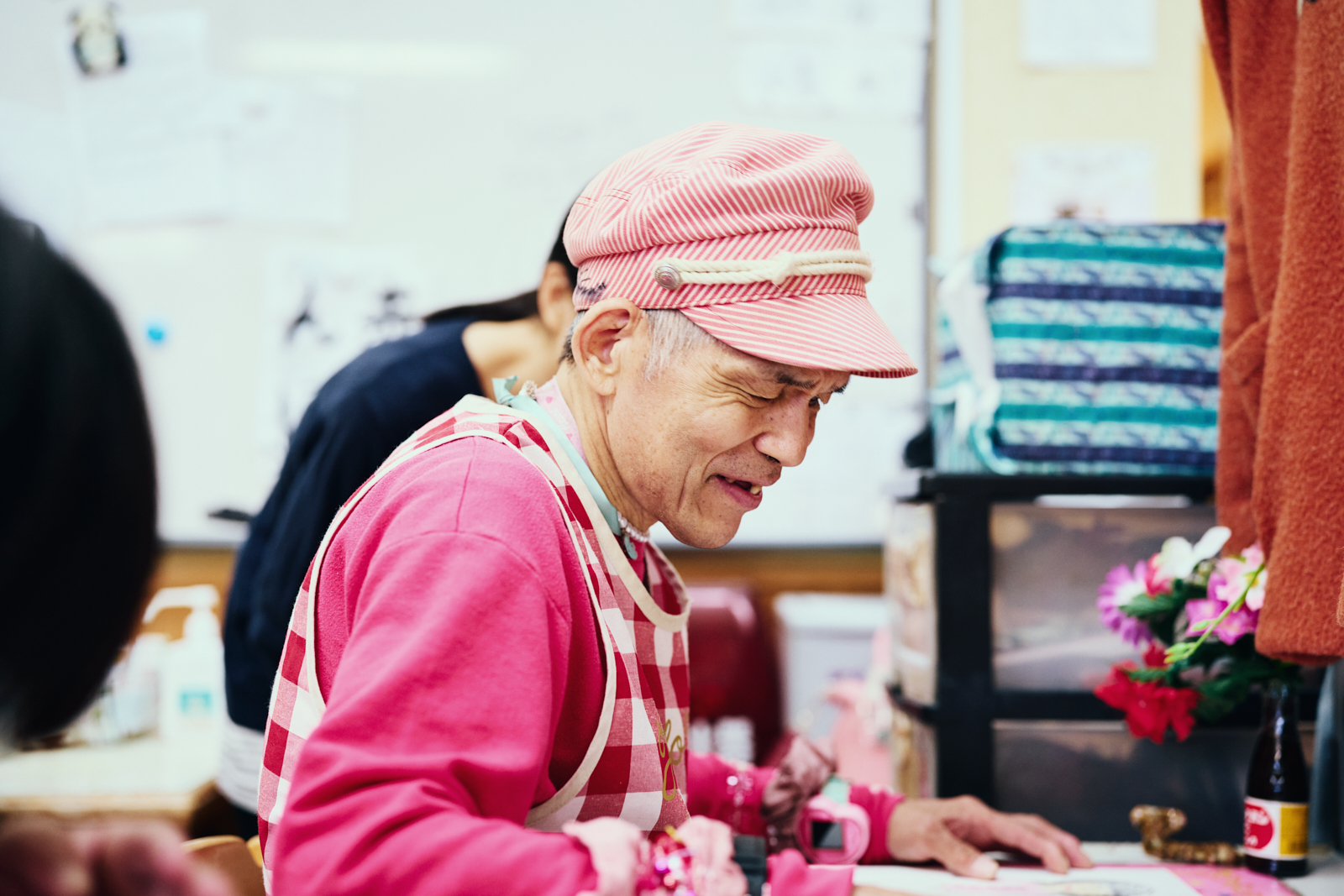【写真】社会福祉法人 さくらんぼ共生会〈さくらんぼ共生園〉に所属するアーティストの荒木恵二さんが、自身が絵を描く作業机の上に視線を落とし、微笑んでいる横顔