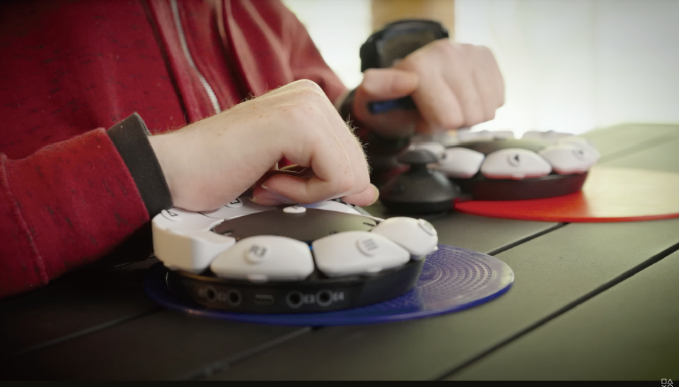 【写真】PlayStation5で使用できるSONY製Access コントローラーを、指を曲げた状態で操作している様子。黒い円盤状のデバイスに白いボタンを自分で設定して配置できるようになっている。
