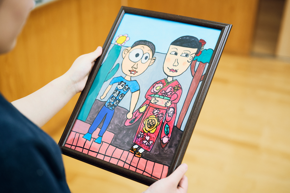 【写真】哲哉さんの姉・志穂さんが手に額装された絵を持っている様子。花柄の赤い振袖を着た志穂さんと、Tシャツ姿の哲哉さんが並んでいる。